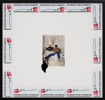 Photograph of a man sitting on a couch in a living room with one foot on a coffee table mounted on a matte in a frame with twelve bumper stickers with the phrase “Describing how a dog was slaughtered” around the frame edge