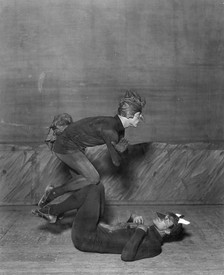 Black and white image of two dancers, dressed as animals, balancing on each other's knees in the ballet "Renard".