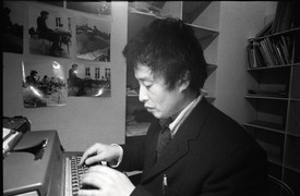 Artist Nam June Paik writing on his typewriter in black and white photo.