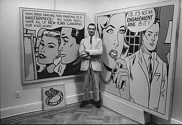 Roy Lichtenstein standing in his studio next to two of his paintings