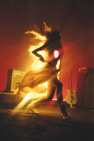 Musician Weyes Blood performs on stage, their entire backside and chest are illuminated